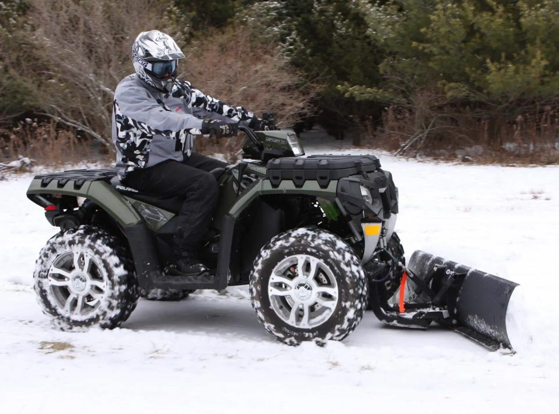 Person on an ATV with snow plow, plowing snow. Outdoors, winter setting.
