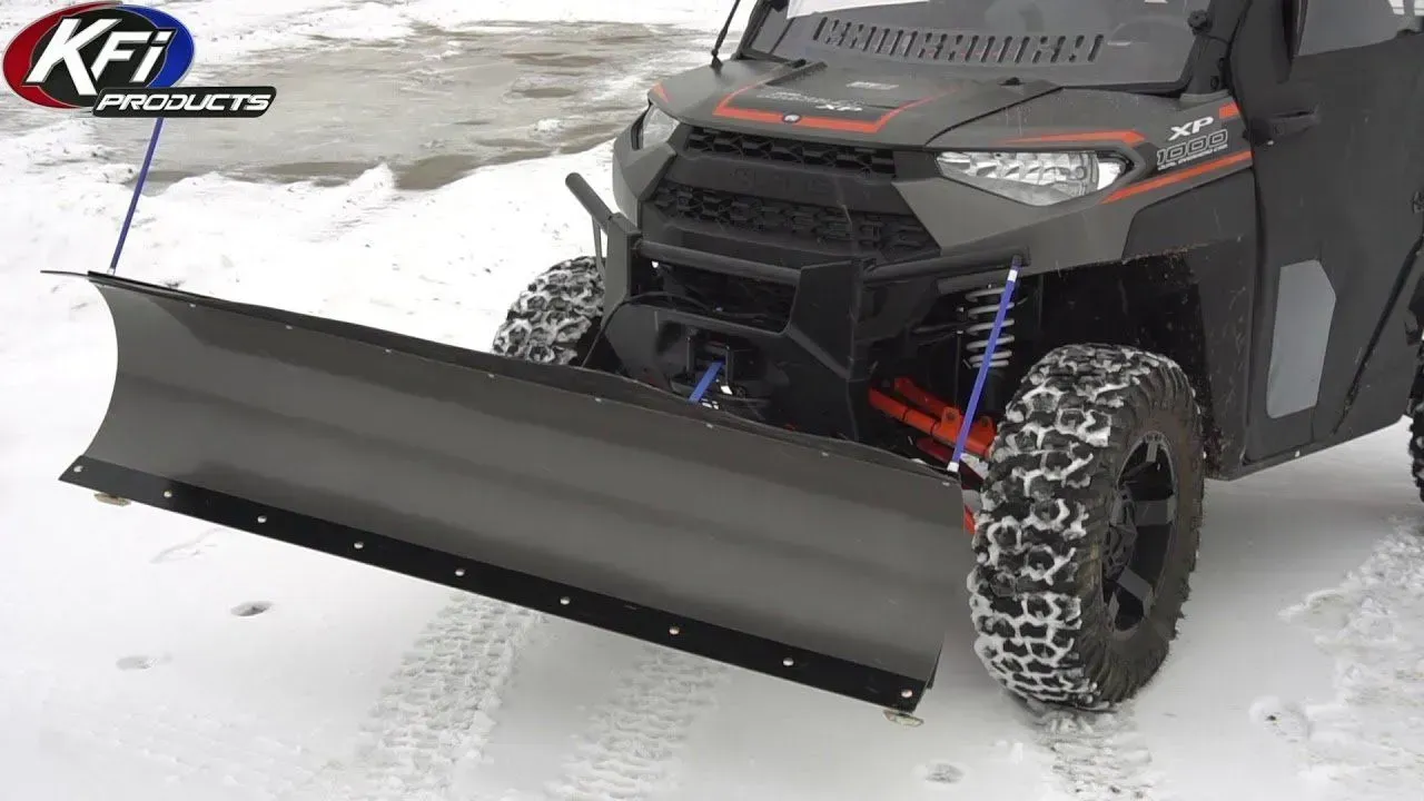 Side-view of UTV with a snowplow attached, clearing snow in a snowy setting.