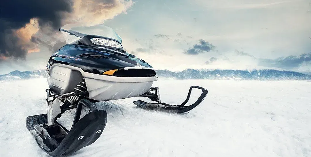 Snowmobile on a snowy plain, with a backdrop of cloudy skies and mountains.